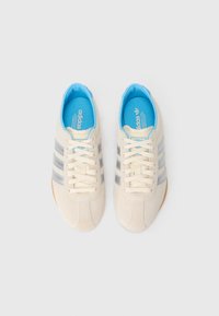 Kremfargede semskede sneakers med tre grå striper, lyseblå innside og gummisåle. Har snøring og en merket såle.
