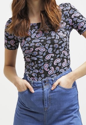Zwart T-shirt met korte mouwen met een paisleypatroon in roze en blauw. Draagt een lichtblauwe denimrok, die een getailleerd ontwerp laat zien.