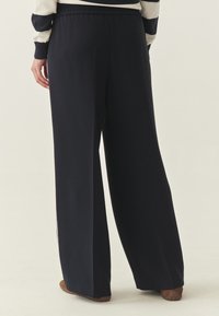 Pantalon large en tissu bleu marine avec une taille élastique, présentant une texture lisse et une silhouette droite. Les accents incluent des plis légers.