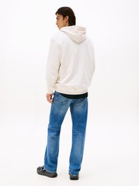 Cremfarbener Kapuzenpullover mit lässigem Schnitt, kombiniert mit hellblauen Straight-Leg-Jeans und schwarzem Schuhwerk. Einfaches, nahtloses Design.
