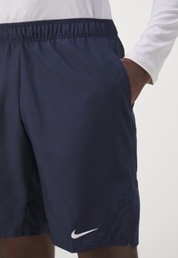 Pantalones cortos deportivos en color marino con una cinturilla elástica, bolsillos laterales y un pequeño logo de Nike en blanco en la parte inferior izquierda delantera. Textura suave.