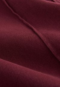 Bordeaux stof med et struktureret, ribbet mønster, der viser bløde, luksuriøse fibre og subtile dimensionelle folder.