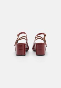 Talons slingback en cuir verni rouge avec un talon épais, comportant trois sangles ajustables et une finition lisse.