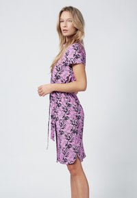 Abito floreale rosa con maniche corte, vita con cordoncino e spacchi laterali. Il design presenta motivi di foglie nere su un tessuto leggero.