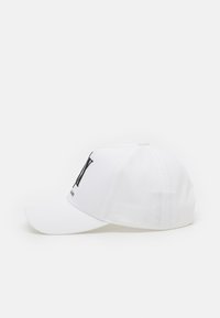 Cappello da baseball bianco con visiera curva, realizzato in cotone. Presenta un logo nero sulla parte frontale e una silhouette strutturata.