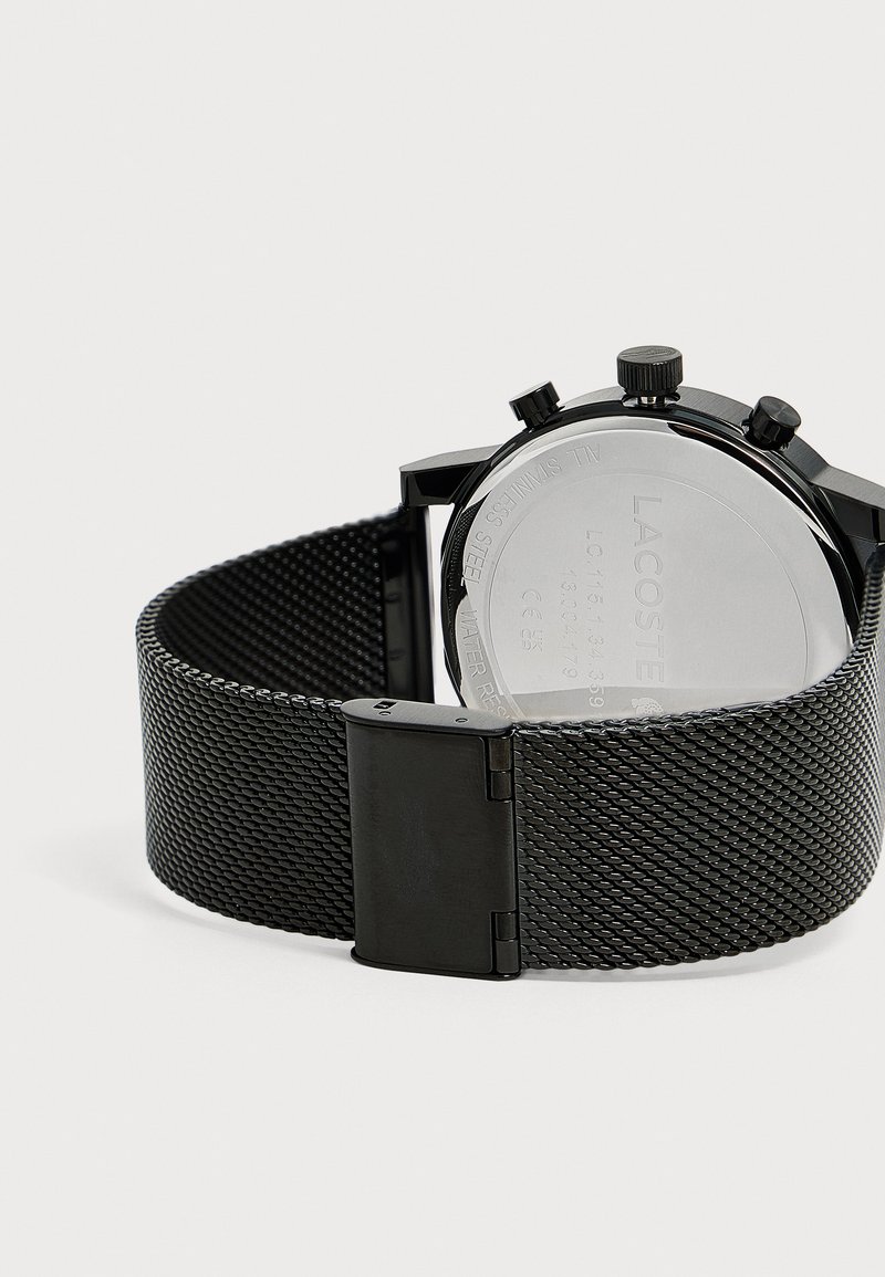 Bracelet de montre en métal noir en maille avec fermoir en acier inoxydable, fixé à une montre avec un fond visible et trois boutons de contrôle.