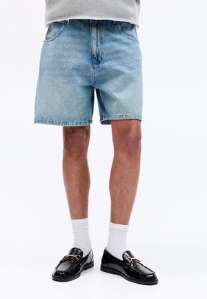 Light blue denim shorts with a relaxed fit, frayed hem, and five-pocket design, paired with black loafers and white crew socks.