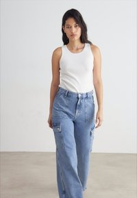 Hvit stripete tank topp og lyseblå overdimensjonerte denim cargo bukser med sidelommer. Stoffet ser mykt ut med en avslappet passform.