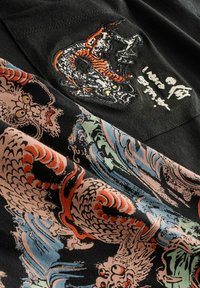 Schwarzes Stoff-T-Shirt mit bunten Drachen- und Wellenmotiven. Verfügt über aufwendige Stickereien und eine glatte Textur. Auffällige Designelemente sind sichtbar.