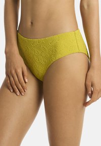 Perizoma giallo in pizzo con motivo floreale, caratterizzato da una texture liscia e copertura moderata. Vita accentuata e bordi morbidi.