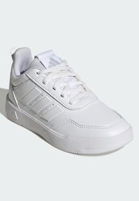 Zapatillas deportivas blancas con cuero sintético y paneles de malla, suela texturizada, diseño clásico con cordones y tres rayas diagonales en el lateral.