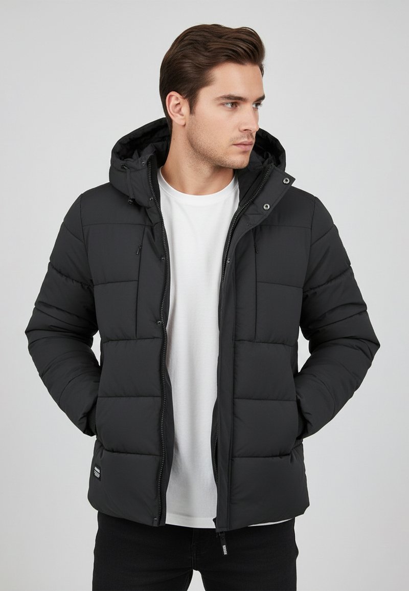 Black puffer jacket with a hood, quilted design, front zipper, two side pockets, and a label on the lower hem. Worn over a white shirt.