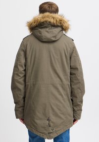 Parka vert olive avec une capuche doublée de fourrure, dotée d'un dos haut, d'une patte de boutonnage à l'avant et de fentes latérales. Fabriquée en tissu durable pour plus de chaleur.