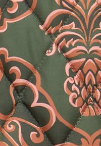 Quilted fabric featuring a green background with a floral design in shades of pink and brown, showcasing diamond patterns and smooth texture.