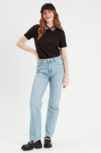 Black short-sleeve shirt with a decorative collar, light blue high-waisted jeans, black chunky shoes, and a black cap.