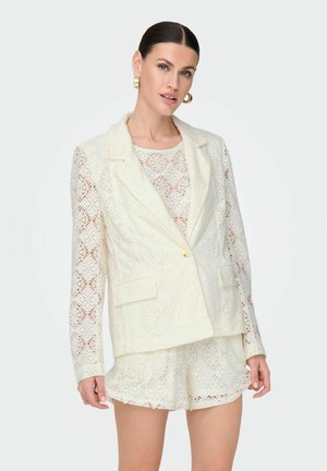 Witte kanten blazer met een sjawlnek, een enkele knoopsluiting en twee voorzakken. Gecombineerd met een bijpassende kanten top en shorts.