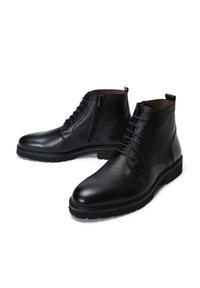 Stivali ankle in pelle nera con finitura textured, lacci frontali e zip laterale, dotati di una suola in gomma robusta e cuciture a contrasto.