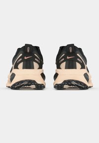 Chaussures de sport noires et beiges avec une tige texturée, des panneaux en maille et un talon proéminent. Présentent des accents roses et une semelle extérieure à motif.