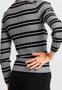 Haut à manches longues à rayures noires et blanches avec tissu texturé, coupe ajustée et détail froncé aux épaules et aux poignets.