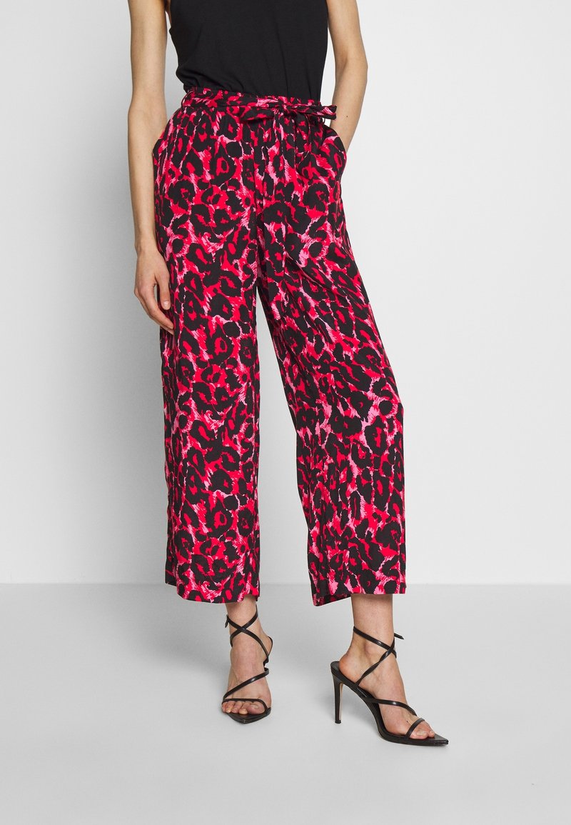 Hose mit weitem Bein im rosa und schwarzen Leopardenmuster, mit passendem Kordelzugbund, kombiniert mit schwarzen Riemchen-High Heels.