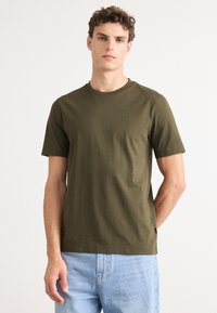 T-shirt en coton vert olive avec un col rond, des manches courtes et un petit logo en relief sur la poitrine. Texture lisse, coupe décontractée.