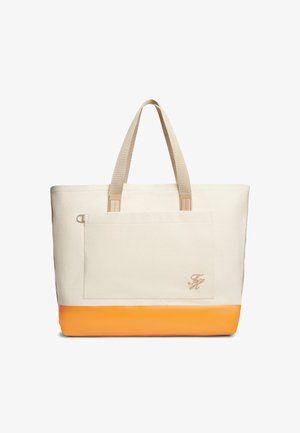 Duża beżowa torba na ramię z płótna z pomarańczowym dnem, beżowymi uchwytami, przednią kieszenią i małymi haftowanymi inicjałami na rogu kieszeni.