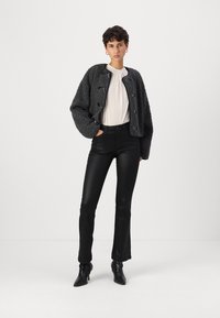 Veste courte grise texturée avec des boutons noirs, associée à un pantalon noir ajusté et des bottines noires. Blouse blanche unie en dessous.