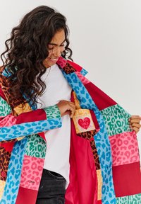 Farebný patchwork kabát s rôznymi zvieracími potlačami v ružovej, modrej, zelenej a červenej farbe. Vo vnútornej vrecku sa nachádza štítok s textom v tvare srdca.