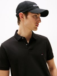 Svart polo-skjorte med strukturert stoff og en treknappslukking, med en liten brodert logo. Svart caps med hvit skrift.