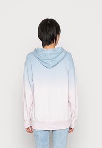 Sudadera con capucha en degradado de azul claro a rosa, con cordón, mangas largas y puños de canalé. Tejido suave con una textura lisa.