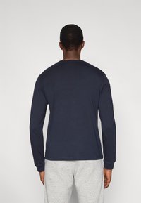 T-shirt a maniche lunghe color blu navy in cotone, con scollo rotondo e vestibilità comoda. Abbinata a pantaloni della tuta grigio chiaro.