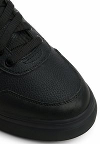 Czarne sneakersy wykonane z teksturowanej skóry i gładkiego materiału syntetycznego. Charakteryzują się okrągłym noskiem, starannym przeszyciem oraz płaskimi czarnymi sznurowadłami.