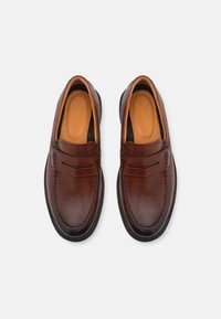 Mocassins en cuir marron avec une finition lisse, intérieur orange contrastant et détails cousus le long des bords. Design minimaliste.