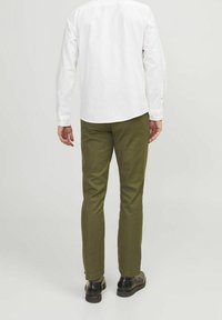 White button-up shirt tucked into olive-green chinos, slim fit. Black shoes and smooth fabric texture with minimal details visible.