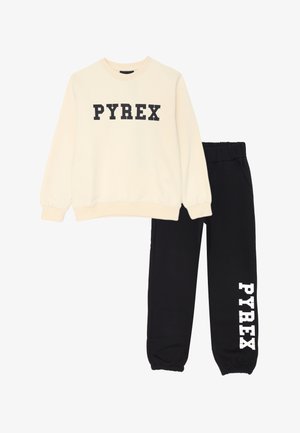 Felpa crema con "PYREX" in lettere nere abbinata a pantaloni neri con "PYREX" in lettere bianche sulla gamba sinistra.