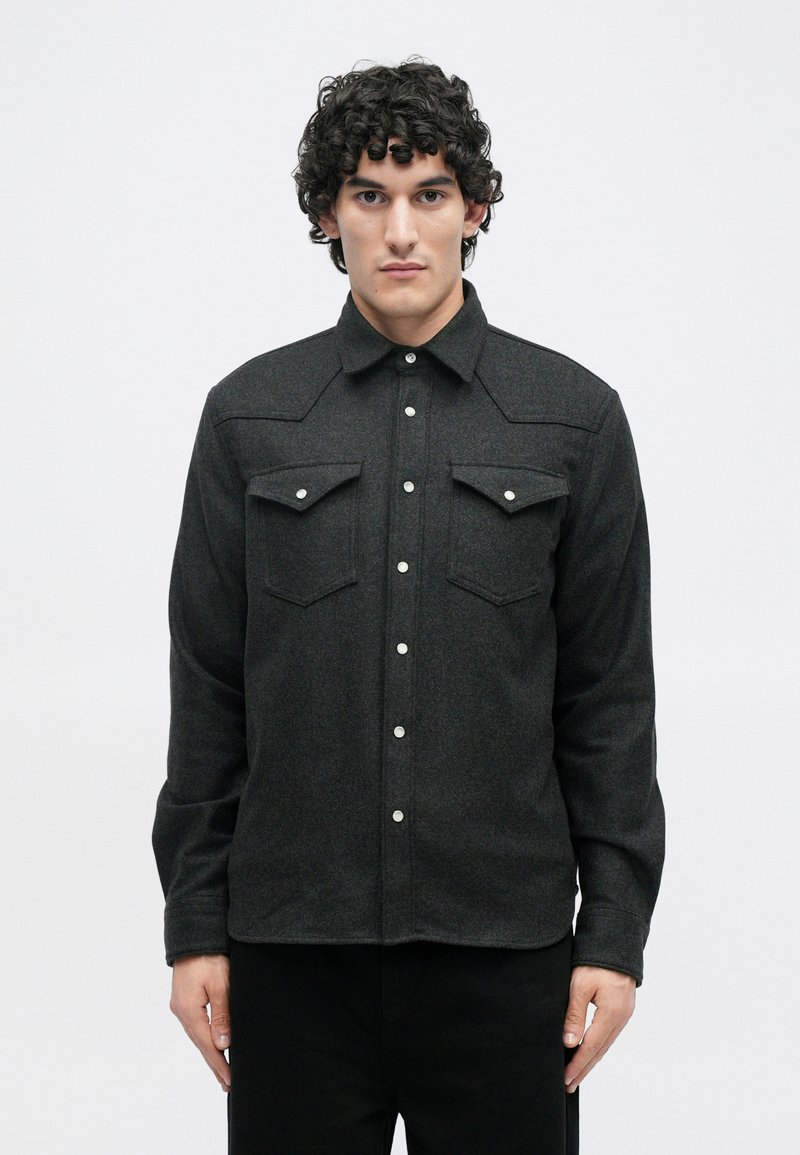 Dark gray flannel shirt with long sleeves, buttoned front, two chest pockets, and a pointed collar. Features white button details.