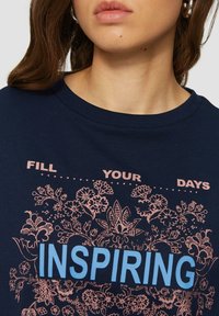 Marineblauw T-shirt met een bloemenontwerp in lichtroze en het woord "INSPIRING" in vette blauwe letters. Rond de hals en met korte mouwen.
