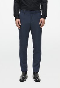 Námořnicky modré kalhoty na míru z texturované tkaniny, s plochým předním dílem, bočními kapsami a slim fit. Nosí se s černými formálními botami.