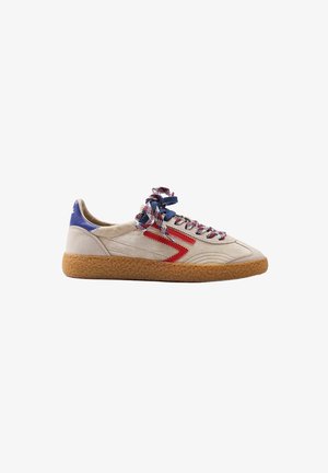 Sneaker in camoscio beige con suola in gomma, striscia laterale rossa a zigzag, toppa blu sul tallone e lacci multicolori annodati a fiocco.