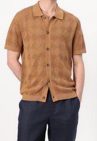 Kortärmad brun stickad polo med ett strukturerat diamantmönster, med knappstängning fram och fast ribbad krage och nederkant.