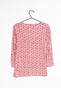Langarmshirt aus pinkem Stoff mit einem runden Muster in Weiß und Lila, mit einem runden Ausschnitt und seitlichen Schlitzen.