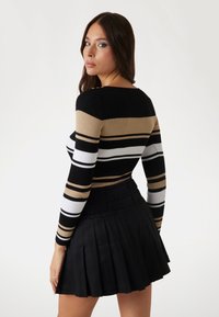 Haut rayé à manches longues noir, blanc et beige avec un col rond, associé à une jupe plissée noire. Texture du tissu lisse.