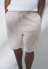 Beige Shorts aus weichem Material mit elastischem Bund und Kordelzug. Verfügt über Seitentaschen und eine glatte, schlichte Textur.