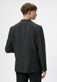 Strukturierter schwarzer Blazer mit taillierter Passform, einem Schlitz auf der Rückseite und Knopfmanschetten. Glatter Stoff mit dezentem Musterdetail.