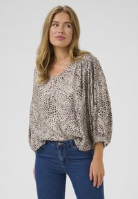 Animal print blouse with a V-neck, long puffed sleeves, and soft, textured fabric in beige and brown tones, paired with blue jeans.