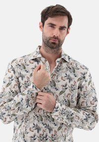 Camicia a stampa floreale in tessuto leggero, caratterizzata da motivi botanici verdi, blu e marroni. Collo classico e design con bottoni, maniche lunghe.