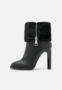 Černé kožené kotníčkové boty na podpatku, s umělou kožešinovou manžetou, stříbrným zipem a lesklým černým podpatkem. Texturovaná podešev pro lepší přilnavost.