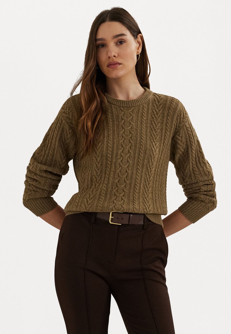 Πλεξιμένο πουλόβερ σε ελαιόλαδο με ανυψωμένα σχέδια καλωδίων, στρογγυλή λαιμόκοψη και ριγωτές μανσέτες, συνδυασμένο με καφέ παντελόνι και καφέ ζώνη.