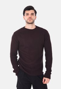 Maglione a coste di colore marrone scuro con scollo rotondo e maniche lunghe, caratterizzato da un tessuto testurizzato e una silhouette aderente.
