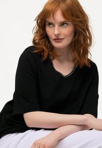 Top corto nero a maniche corte con scollo rotondo e cuciture decorative. Tessuto morbido con vestibilità rilassata.